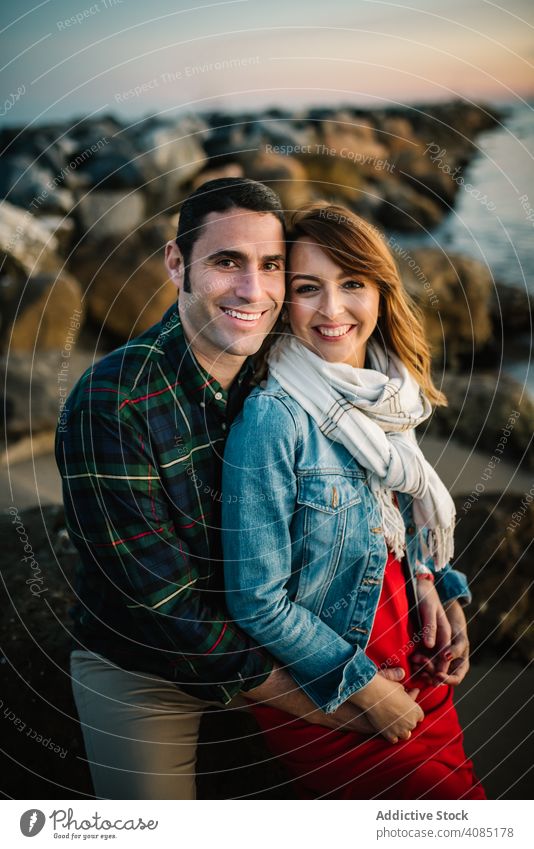 Happy couple sitting on stone pregnant smiling beach love belly adult tender relationship man woman shore boulder rock coast romantic lifestyle leisure rest