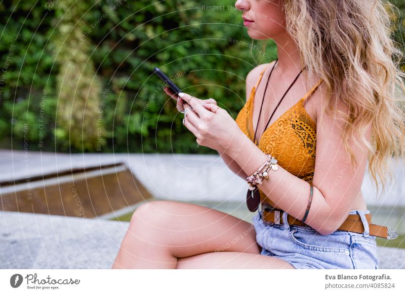 young blonde beautiful woman at the street using mobile phone and smiling. Lifestyle outdoors. Summertime, Green background smart urban happy people run modern