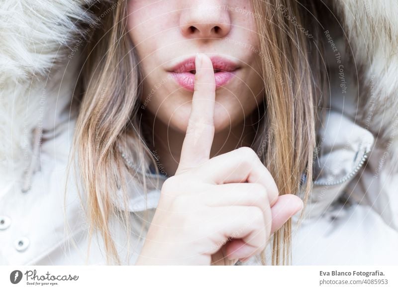 silence, gesture and beauty concept - close up portrait of a young woman holding finger on lips happy beautiful girl lifestyle fashion coat nature park