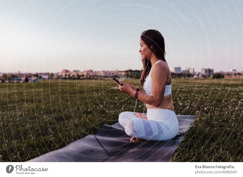 young beautiful asian woman relaxed after her yoga practice listening to music on earphones and mobile phone. Yoga and healthy life concept summer happy