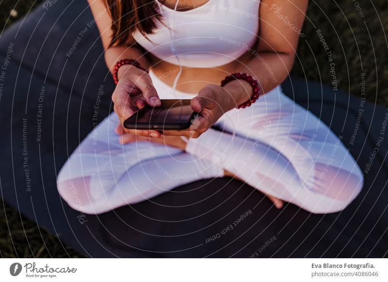 unrecognizable asian woman relaxed after her yoga practice listening to music on earphones and mobile phone. Yoga and healthy life concept young summer happy