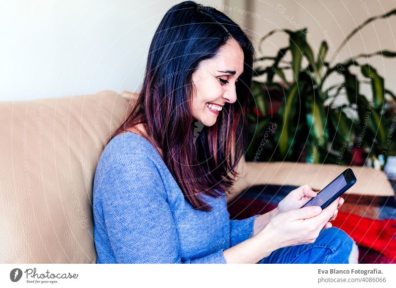 young woman sitting at cozy home sofa and using modern smart phone device, female hands typing text message. social networking concept internet hi-tech day