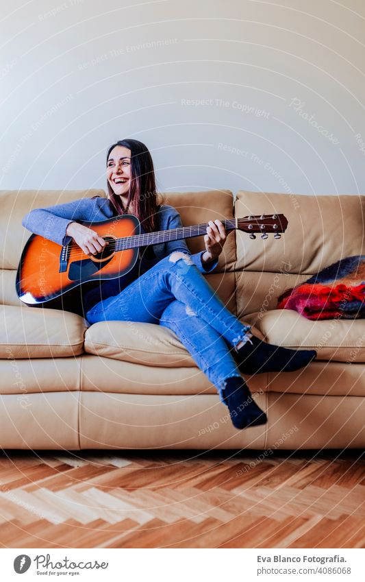 Young beautiful woman playing guitar standing on the sofa. Music concept portrait drive home inspiration bedroom band electric rock expression female freedom
