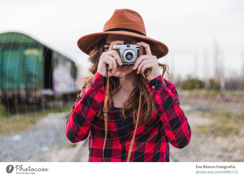 young beautiful woman wearing casual clothes and a hipster hat taking a picture with a vintage camera. Outdoors city background. Lifestyle. happy photo adult