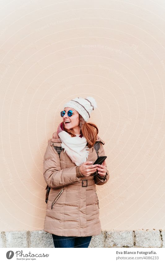 woman using mobile phone over yellow wall background. Technology and winter concept outdoors city technology lifestyles sunglasses modern app video working call