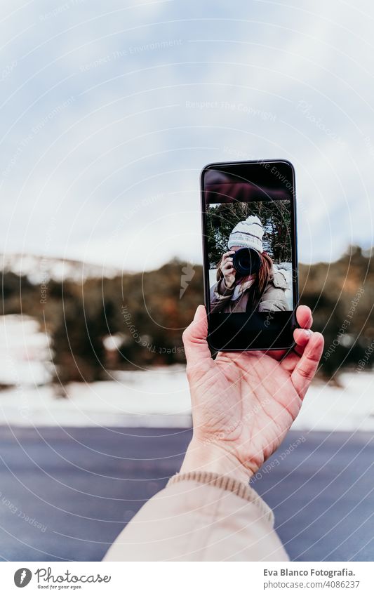 woman at the mountain taking a self portrait on mobile phone with camera. Winter season photographer selfie holding hand snow winter forest lifestyles hat