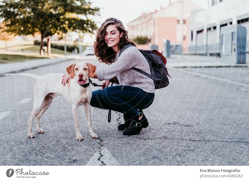 young woman and her dog outdoors walking by the street. autumn season park love pet owner sunny beautiful happy smile mixed race purebred breed hug backpack