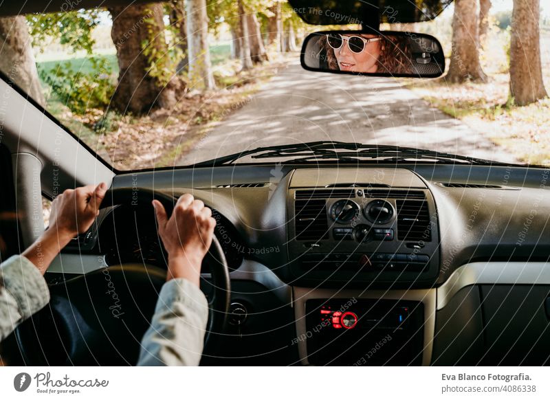 young beautiful woman driving a car. travel concept. view from inside. path of trees road sunny sunglasses traveling wheel drive hire sharing new traffic