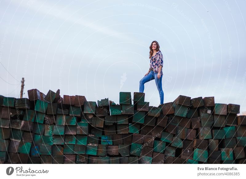 portrait of a young beautiful woman wearing casual clothes, standing on a mountain of green wood blocks background and smiling. Outdoors lifestyle. youth