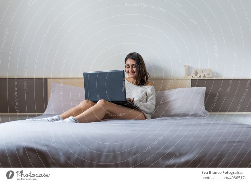 young woman sitting on the bed working with laptop coffee lifestyle computer cup casual internet business networking typing social house home bedroom morning
