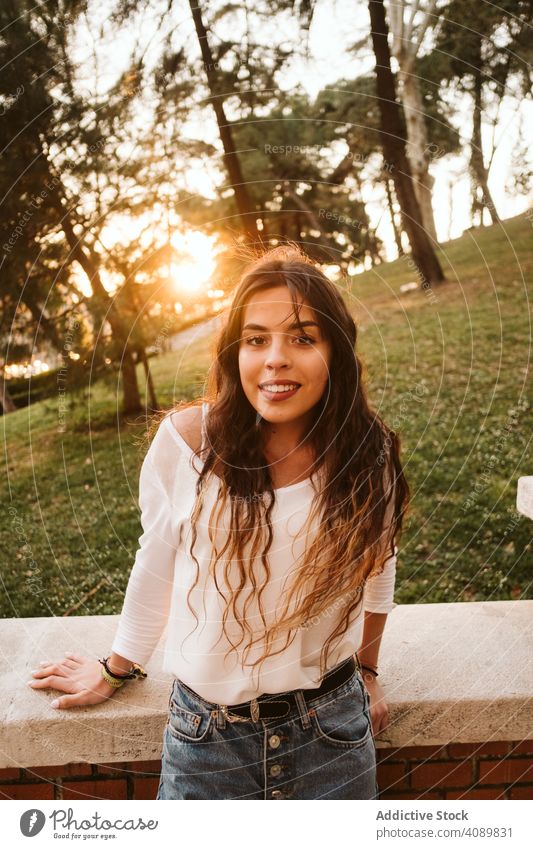 Cheerful young woman in street portrait park city border leaning smiling sunny daytime carefree lifestyle leisure female casual cheerful happy joy fence summer