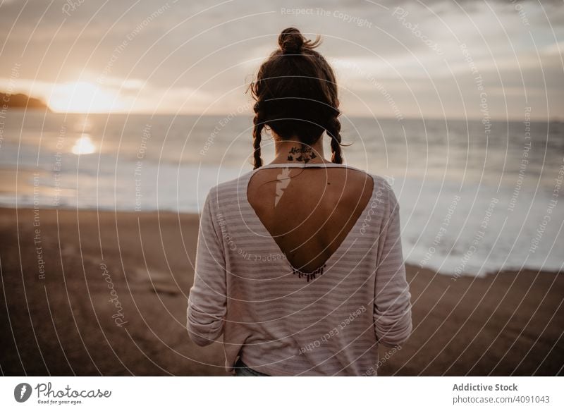 Back view of anonymous female friends in swimwear and summer clothes  embracing while standing on stony coast against waving sea during vacation  together in Puerto Escondido stock photo