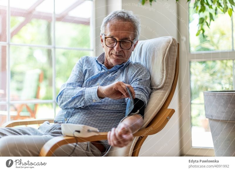 Senior man using medical device to measure blood pressure senior elderly grandfather old pensioner retired retirement aged mature home house male people