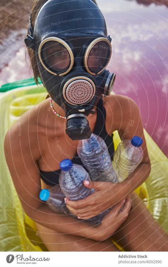 Female in gas mask and with plastic bottles in lake water woman environment sea respirator trash air mattress concept social pink swimsuit red lagoon recycle