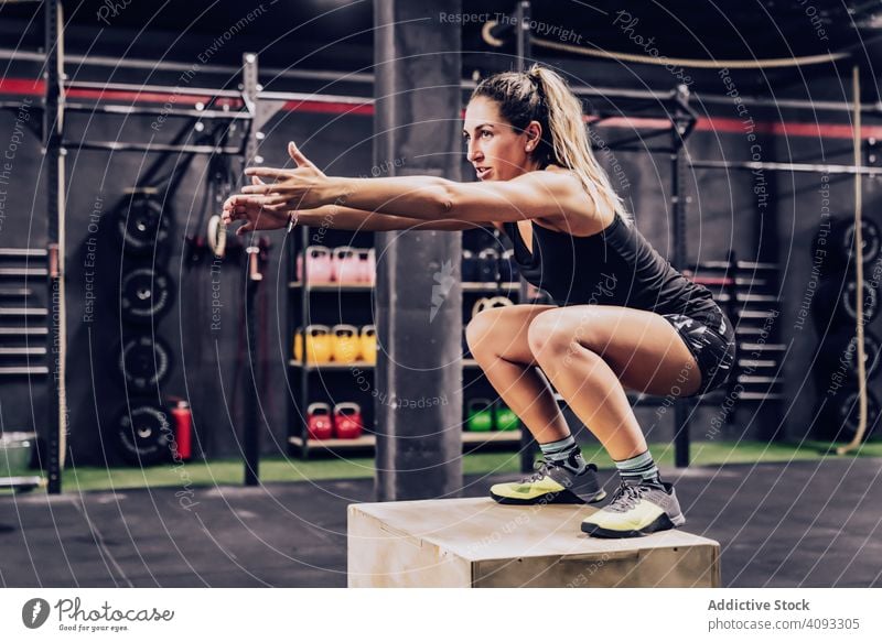 Athletic woman jumping on box to improve stamina in gym trainer workout muscular exercise athletic client help fellow squatting sport club bodybuilder athlete