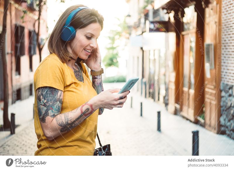 Inspired woman in headphones listening to music on smartphone on street hipster cool using streaming wireless attentive inspired tattooed stand sunny city town