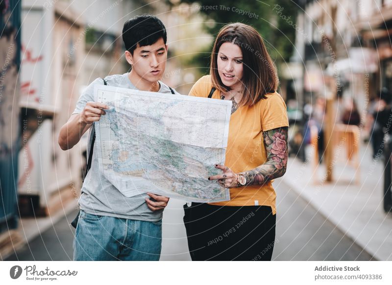 Joyful multiracial tourists checking map and standing on urban street joyful fun lost laugh city direction holding smile search multiethnic asian diverse