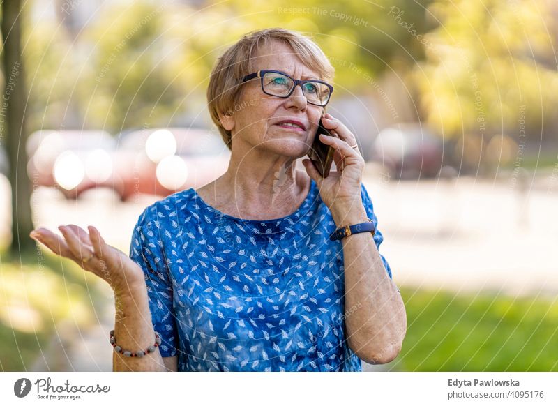 Stressed senior woman using mobile phone outdoors people mature casual female Caucasian elderly old grandmother pensioner grandparent retired retirement