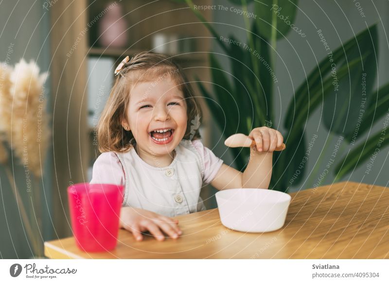 A little girl eats porridge from a white bowl, a girl has breakfast sitting at the table. Healthy breakfast, healthy food child eating plate baby cute childhood