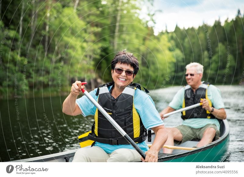 Happy mature couple in life vests canoeing in forest lake. Sunny summer day. Tourists traveling in Finland, having adventure. active activity beautiful discover