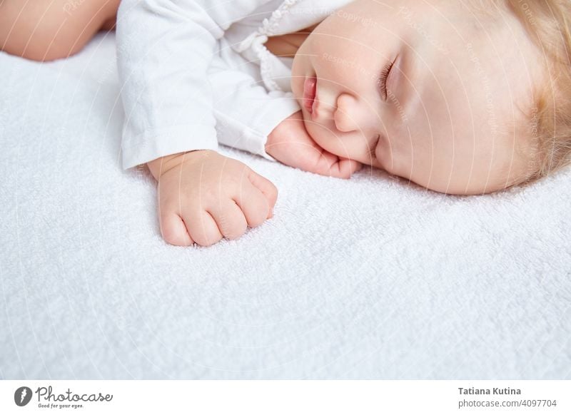 Cute baby sweetly sleeps on white bed linen in white clothes. Close-up. Beautiful healthy soft skin, long eyelashes. child cute little kid portrait small infant