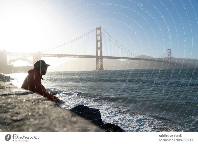 Tourist gazing at scenic bridge at peaceful bay tourist gaze sea coast man stand distant iron sun rays wave pier usa golden gate young adult mist landmark