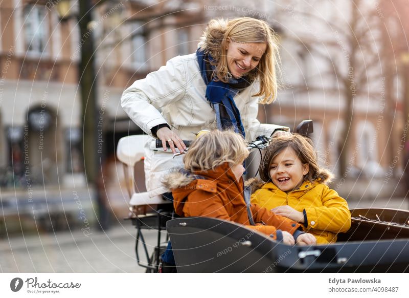 Mother checking on her children who is riding in the front section of a cargo bike cycling transport tricycle healthy active bicycle biking modern
