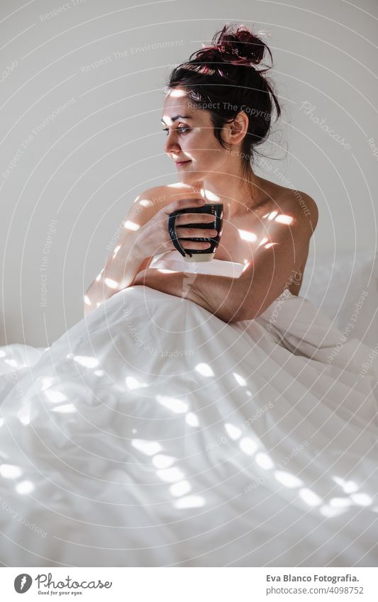 attractive young caucasian woman relaxing well in bed during morning time. Lady enjoys cup of coffee in bedroom breakfast drink beverage hot tea drinking