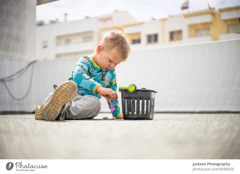 Small boy playing with colorful clothes pegs on the rooftop of his apartment building lockdown game fun toy small roof top covid covid 19 pandemic basket