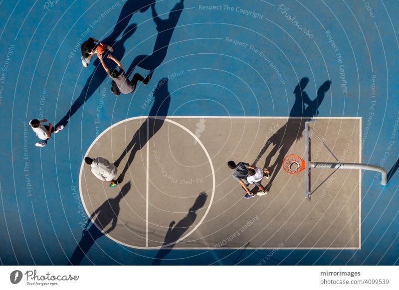 young man playing basketball at dusk or morning light with long shadows high angle bird's eye view netted hoop court b-ball high angle view hoops in city courts