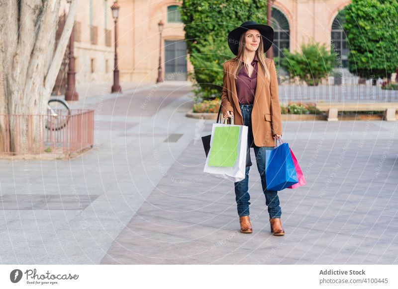 Content female in trendy wear doing shopping at city street woman shopping bags fashionable stroll purchase weekend walking stylish outfit hat casual