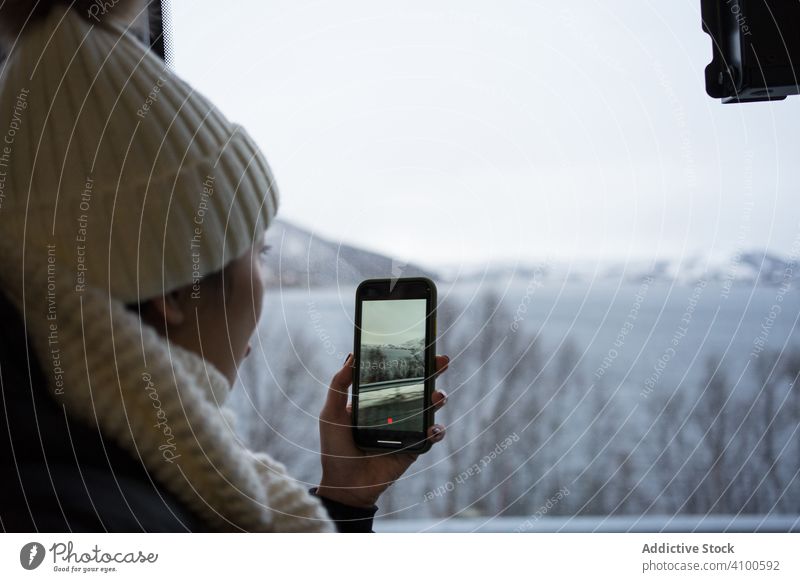 Calm woman recording video with smartphone of wintry scenery while looking out window photography winter norway ersfjordbotn travel shooting cold tourism device