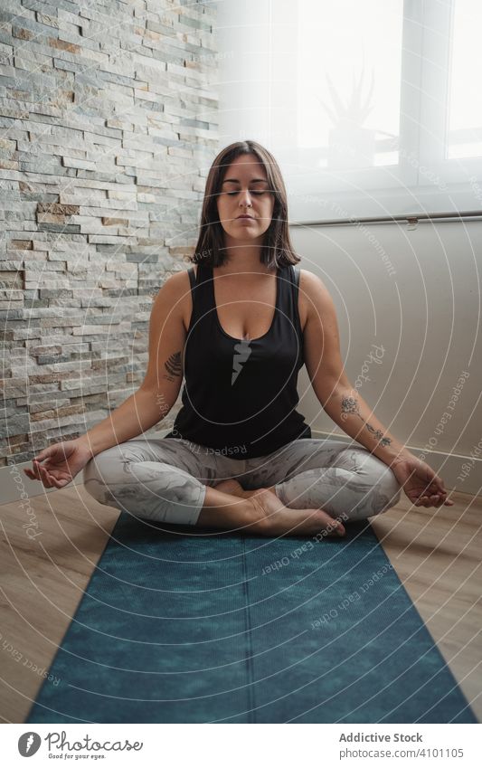 Woman in lotus pose meditating at home woman meditation yoga lotus position mat practicing morning padmasana room relaxation young brunette female sitting