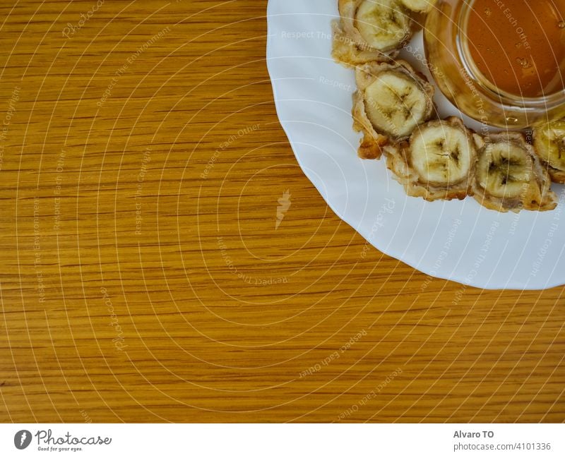 Delicious Fried slices of the ripe plantain and a glass of honey making a beehive on a round wooden plate. Top View plantains dessert banana fritter eat