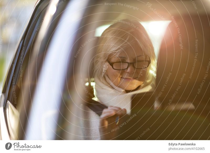Senior woman with smartphone on the back seat of a car people one person senior mature pensioners retiree retired retirement old elderly gray hair caucasian