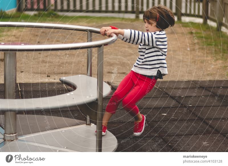 Side view of a little girl propelling a spinning carousel in a playground active activity agility amusement amusing caucasian challenge child child play