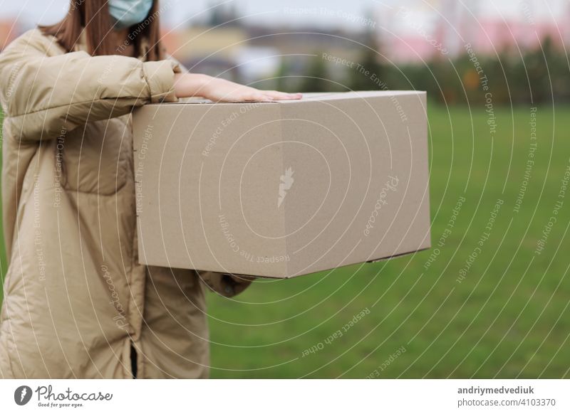 Delivery girl in face medical mask hold empty cardboard box outdoors on a residential complex background. Service coronavirus. Online shopping. mock up.