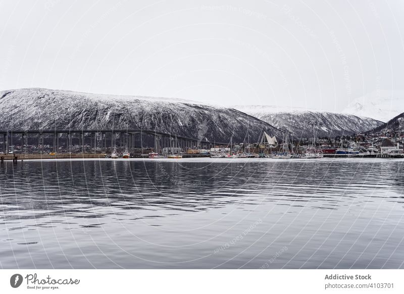 Landscape of sea bay next to big snowy cliff mountain harbor overcast cloud dusk city calm tranquil landscape tourism blue village water nature scenery town