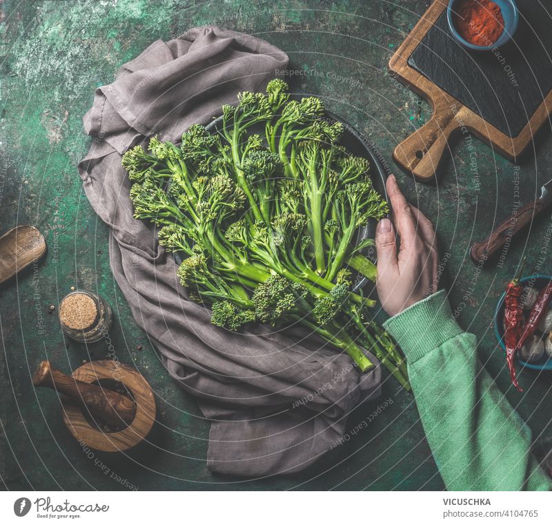 Women hand in green sweatshirt holding wild broccoli on dark rustic background. Top view. Healthy food women top view healthy food preparation kitchen table