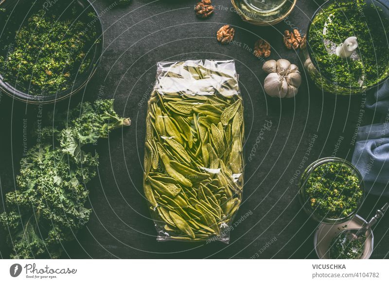 Green pasta in plastic packing on dark kitchen table with kale and other ingredients. Top view green top view rustic brunch noodle nutrition carbohydrate meal