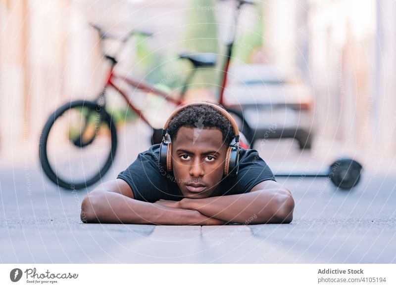 Focused young black male teenager listening to music in street man headphone cool lying asphalt road lifestyle student relax entertainment song youth modern