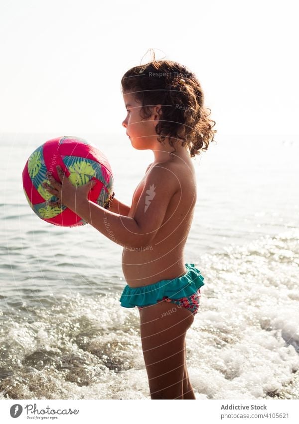 Little girl on beach with a ball play sand sea sit haunches kid summer vacation season child ocean water lifestyle rest relax shore coast joy calm tranquil