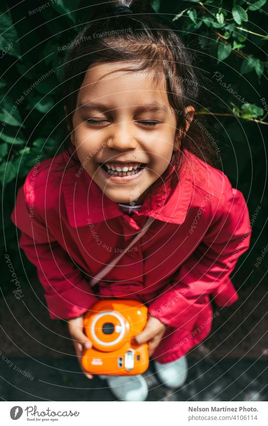 Portrait of a little hispanic girl, wearing a fucsia coat, holding a vintage orange camera childhood people joy amusement holiday playing enjoyment children