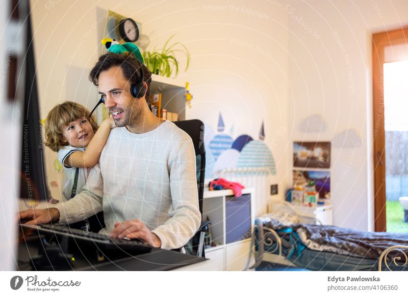 Young man working from home with his little son as a company single father working at home computer busy laptop life balance coronavirus covid social distancing