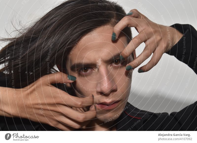 Handsome young man with long brown hair, green painted nails, with penetrating gaze and serious expression, fixed gaze close up attractive beauty