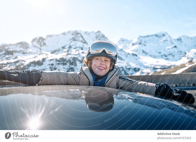 Cheerful boy with raising arms out of car windows snowball winter smile roll resort sunny daytime kid child recreation lifestyle happy cheerful delighted
