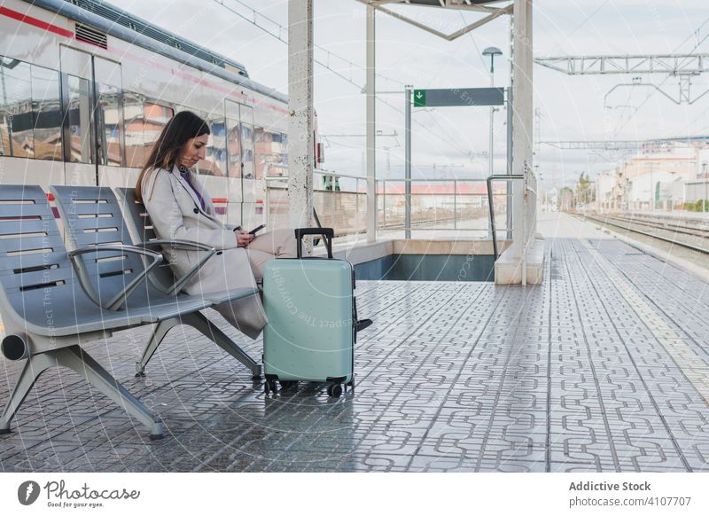 Woman waiting for train and using phone woman station mobile phone travel smartphone holiday suitcase railway bench young transport terminal transportation trip