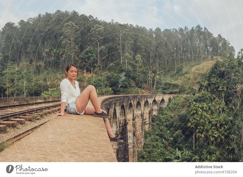 Asian woman sitting on railroad on bridge in tropical landscape travel exotic conetnt tourism relax female casual green forest ethnic tree plant asian sky