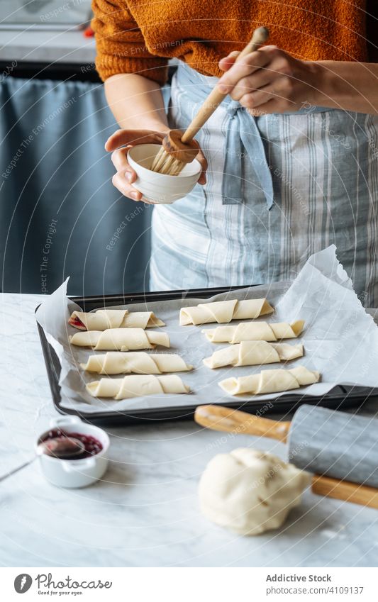Cook holding bowl and brushing croissants in baking sheet on table jam dough rolling rolling pin preparation sliced bakery homemade culinary making sweet