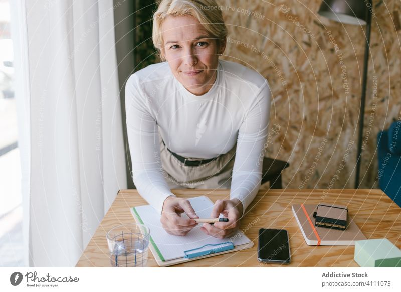 Blond woman writing on clipboard bending on office desk businesswoman note plan write pensive workplace table concentrate information document job smart